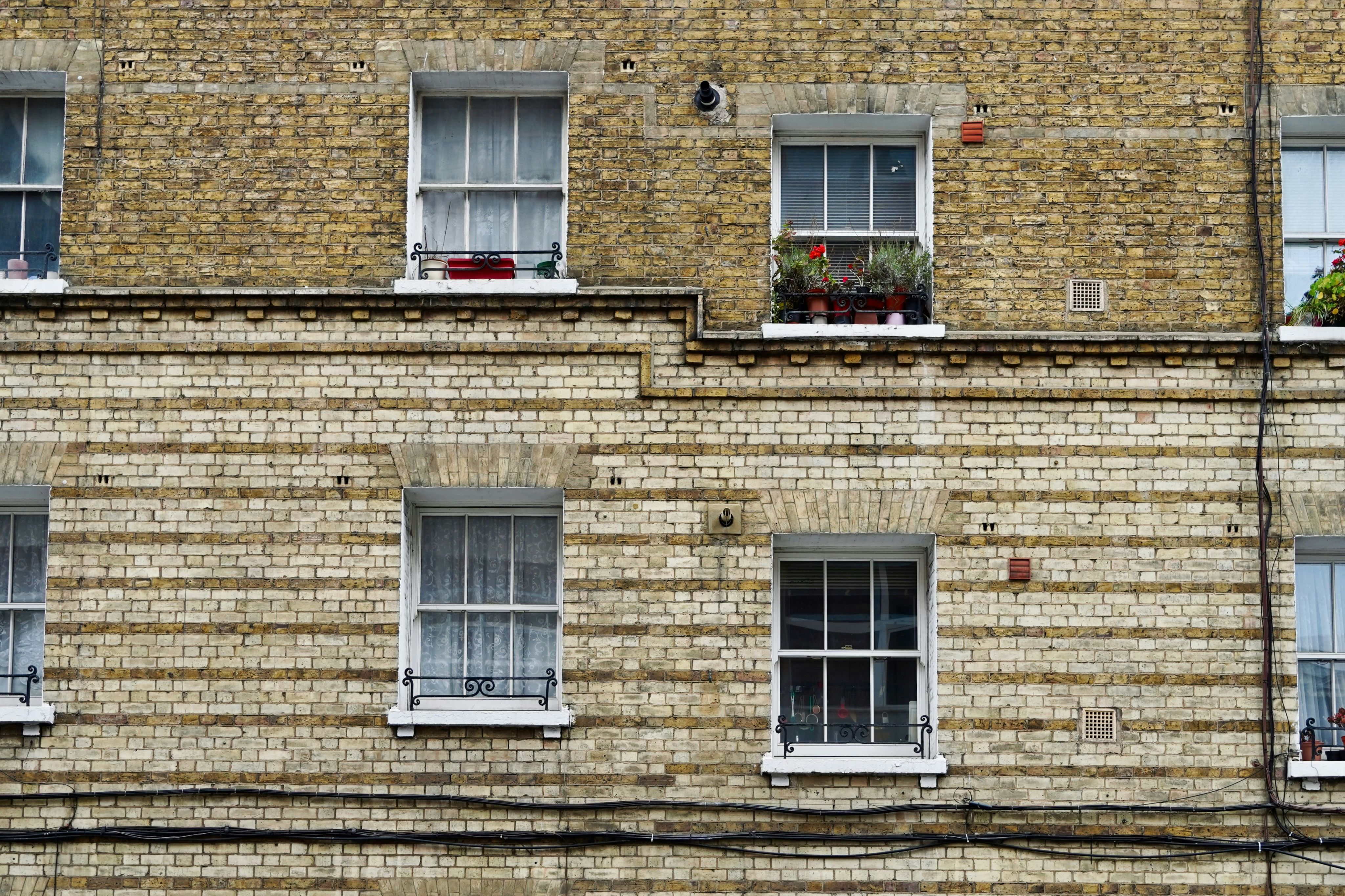 Residential building façade. Four windows across two floors. One with plant pots outside.  