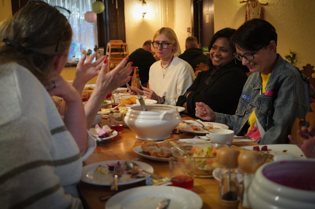 Five people sat around a dinner table talking, alughing and eating