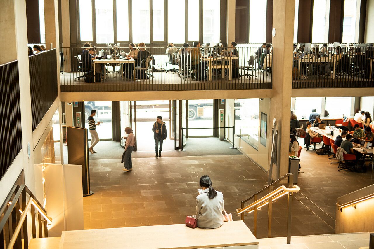 Photo of UCL student centre. Students working on mezzanine level and entering through the door below.
