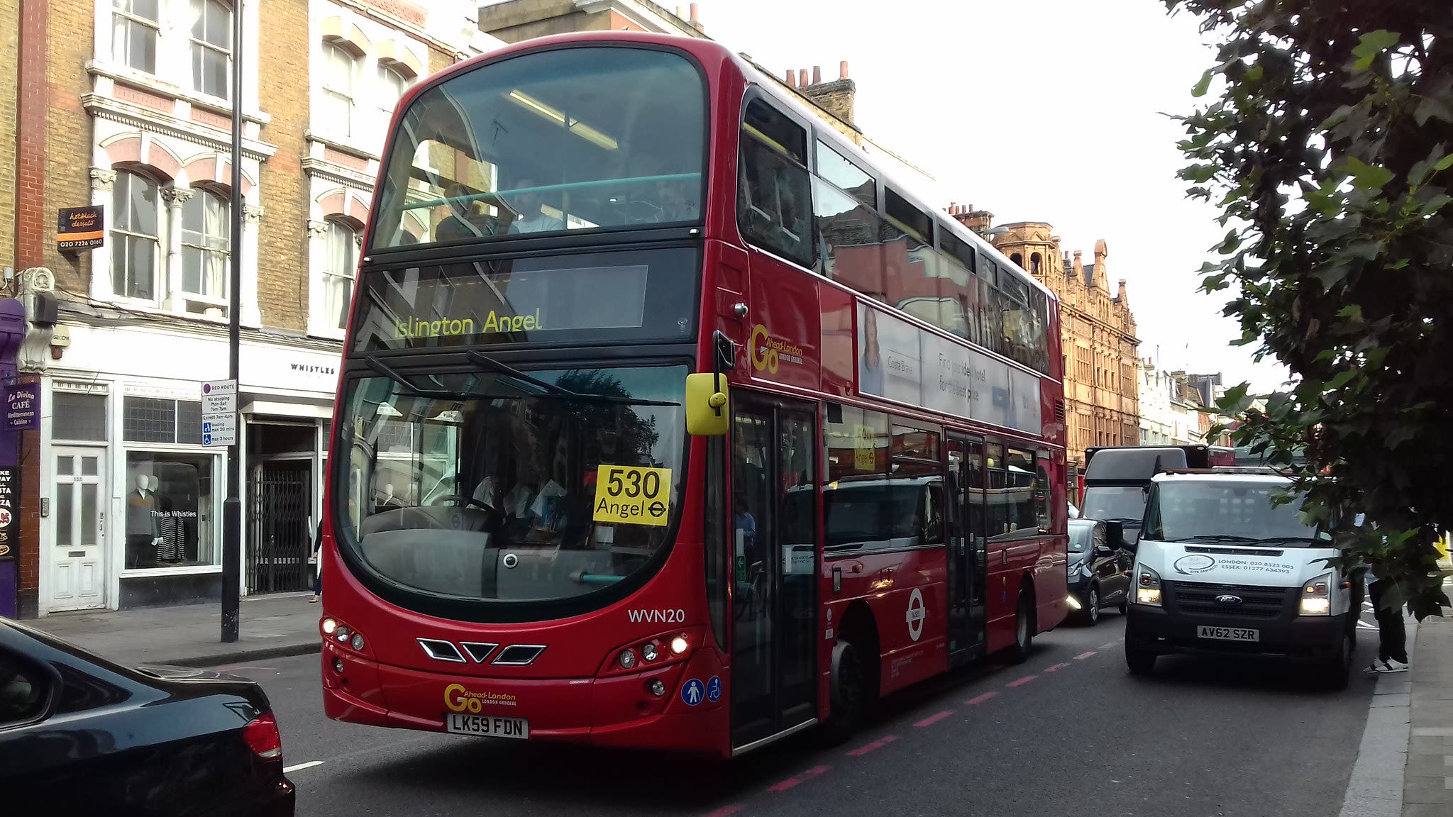 Red bus driving past row of buildings