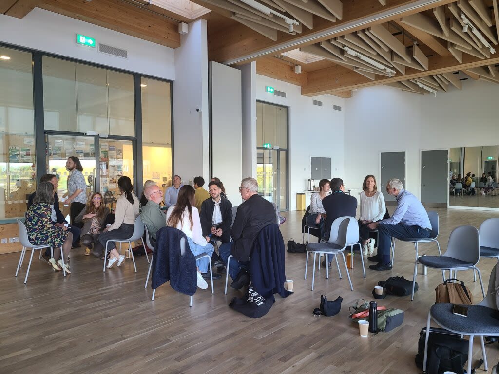 Group of people seated and talking inside a large, bright, open building.