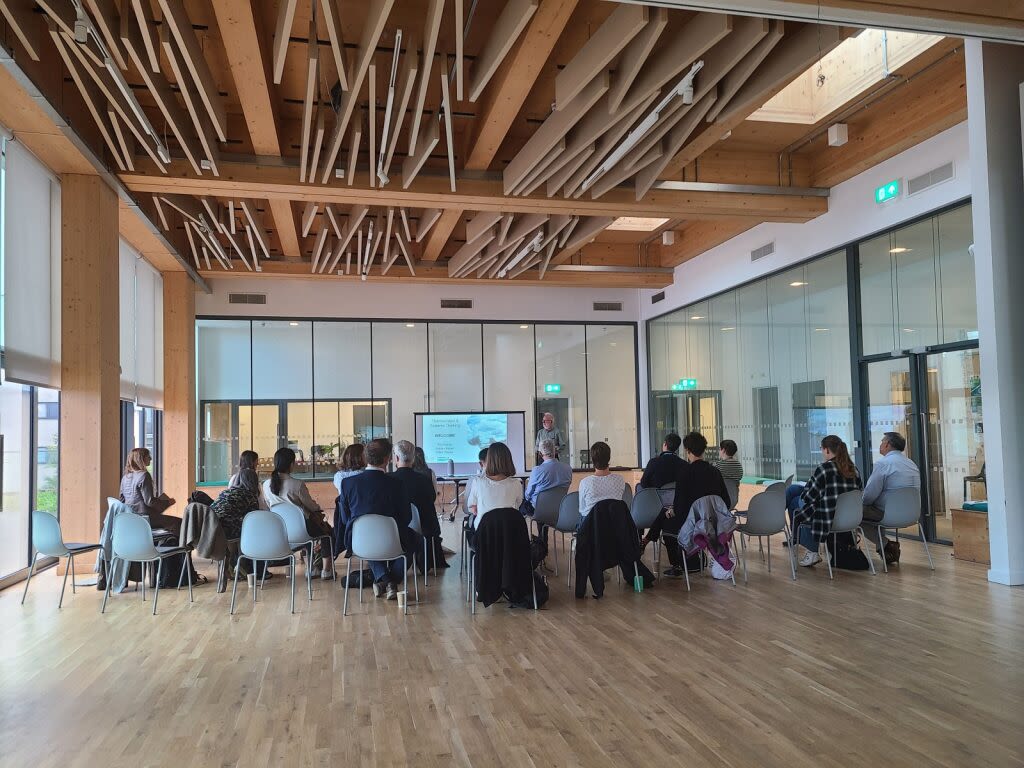 Group of people seated and talking inside a large, bright, open building.